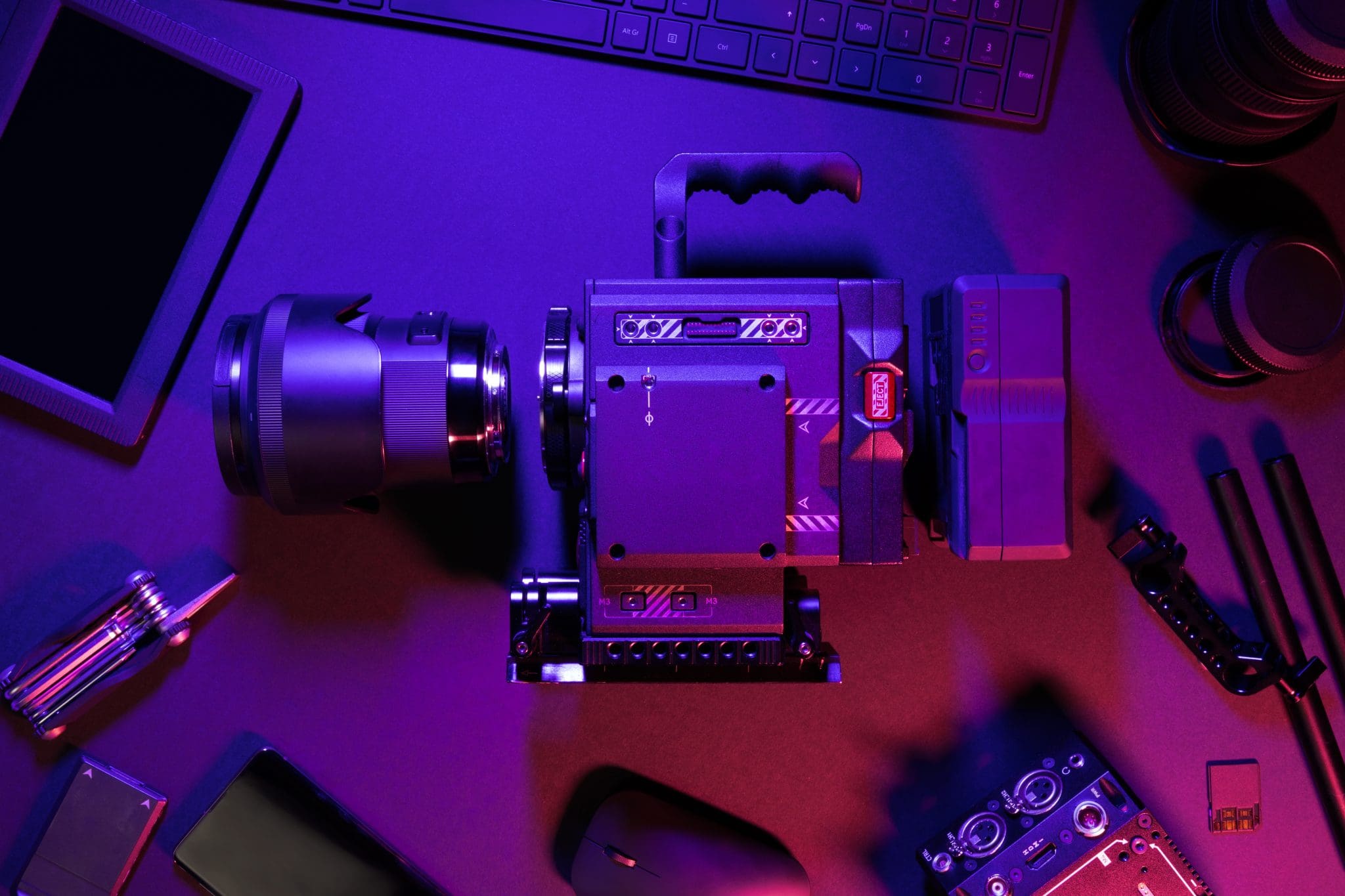 Directly above shot of professional cinema camera and computer parts. Overhead view of various illuminated electronics. Equipment are on colorful table.